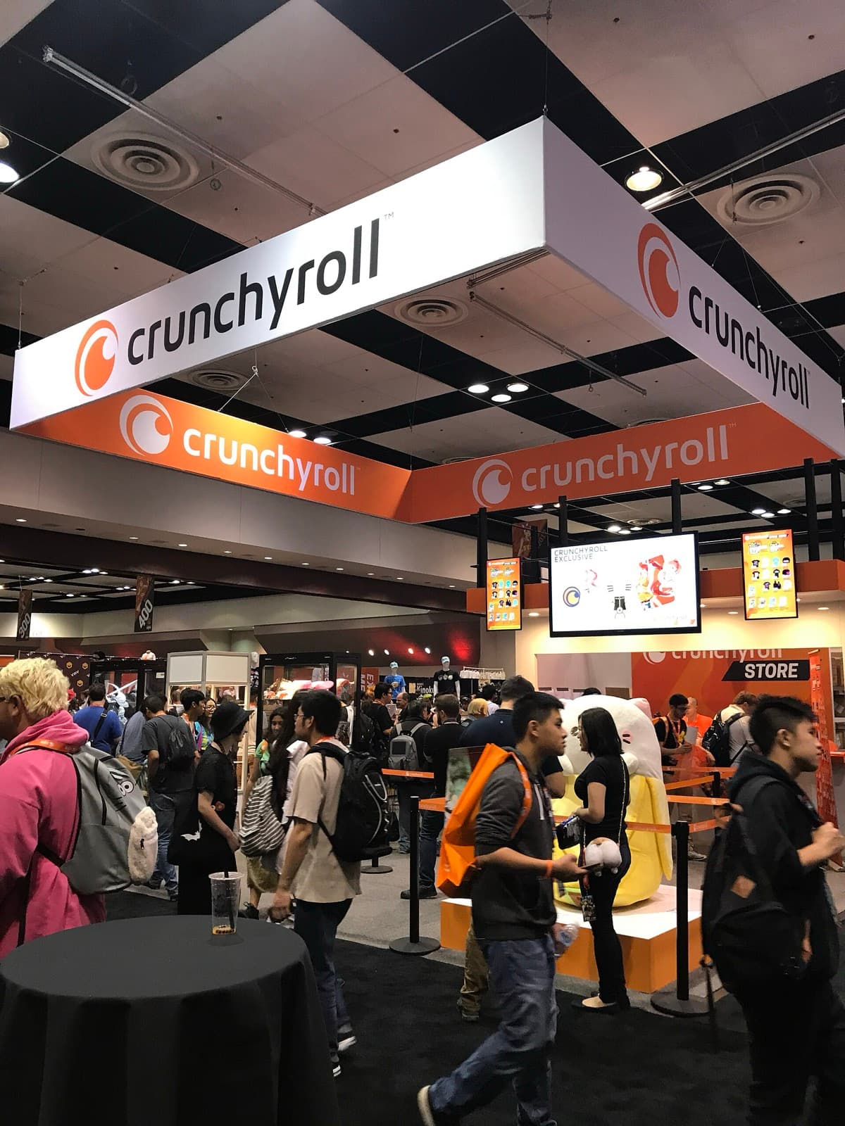 Convention hall with large orange and white Crunchyroll banners above a crowded booth