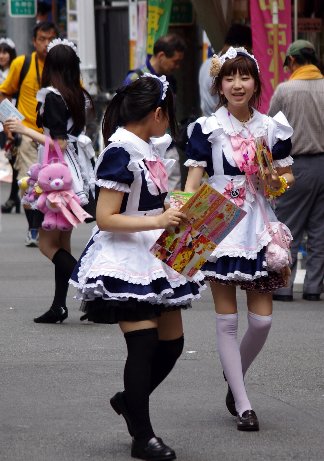 Two young women in frilly maid costumes distributing flyers on a busy street
