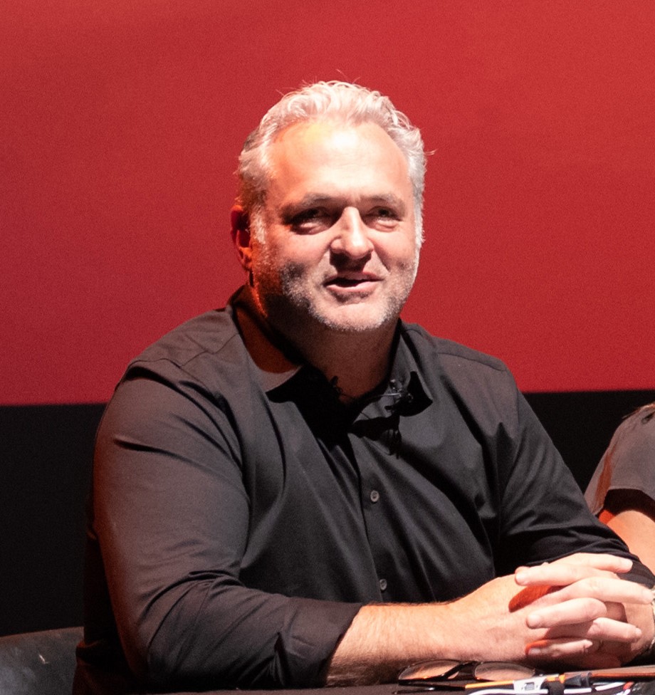 Genndy Tartakovsky seated at a panel table against a red backdrop