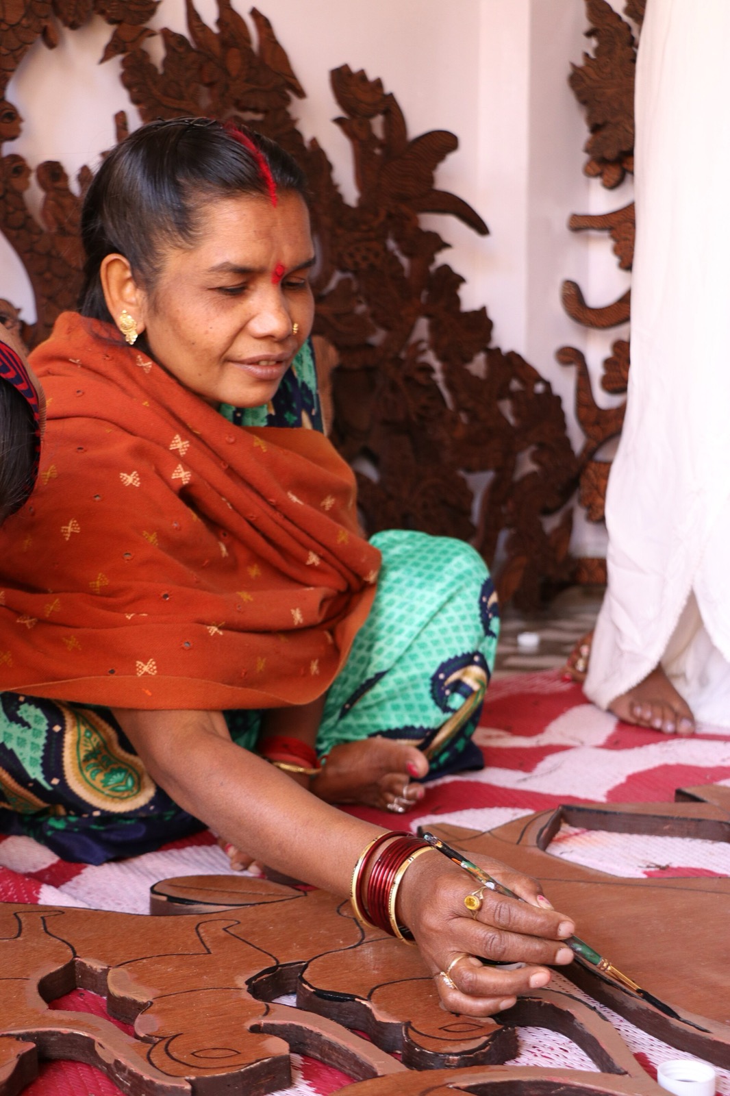 Durgabai Vyam seated on the floor painting a carved wooden panel