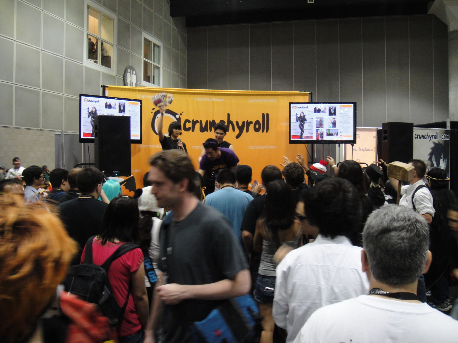 Convention crowd in front of an orange Crunchyroll booth with two video screens