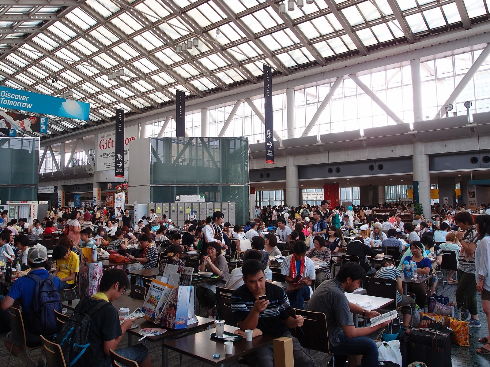 Hundreds of attendees seated and walking in a glass-roofed exhibition hall