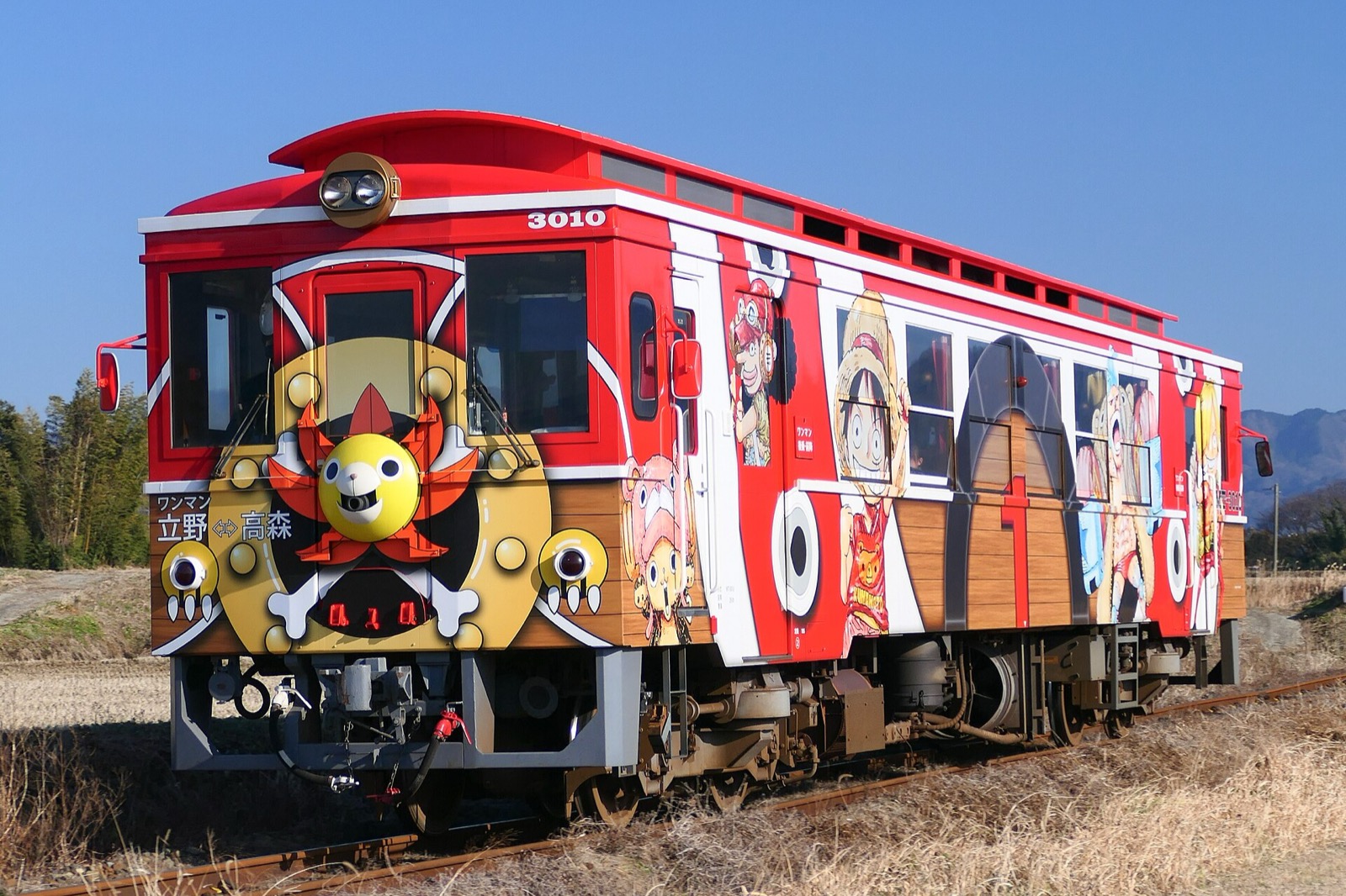 Red railway car decorated with One Piece characters on a rural Kumamoto line