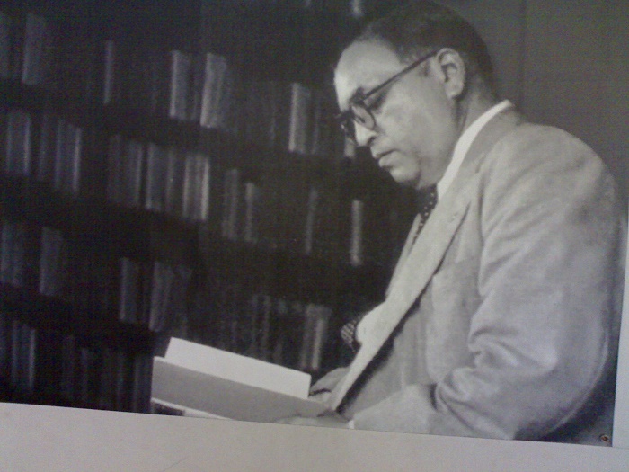 Black and white photo of B. R. Ambedkar reading a book beside a shelf