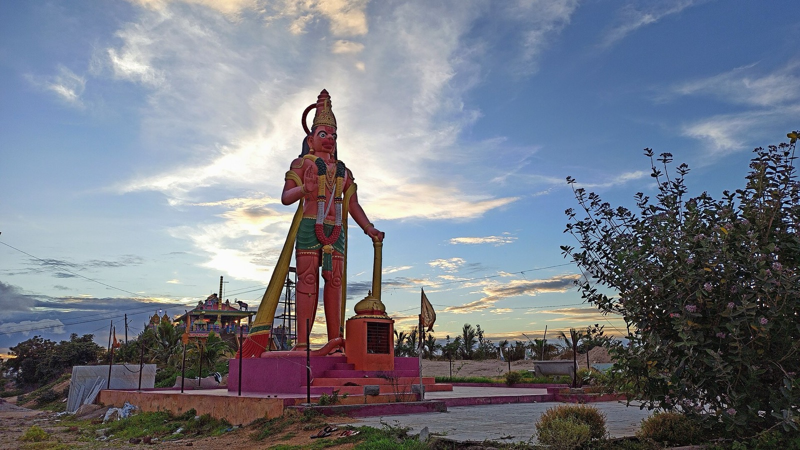 Colourful Hanuman statue with a mace beside a temple against a sunset sky in Hyderabad