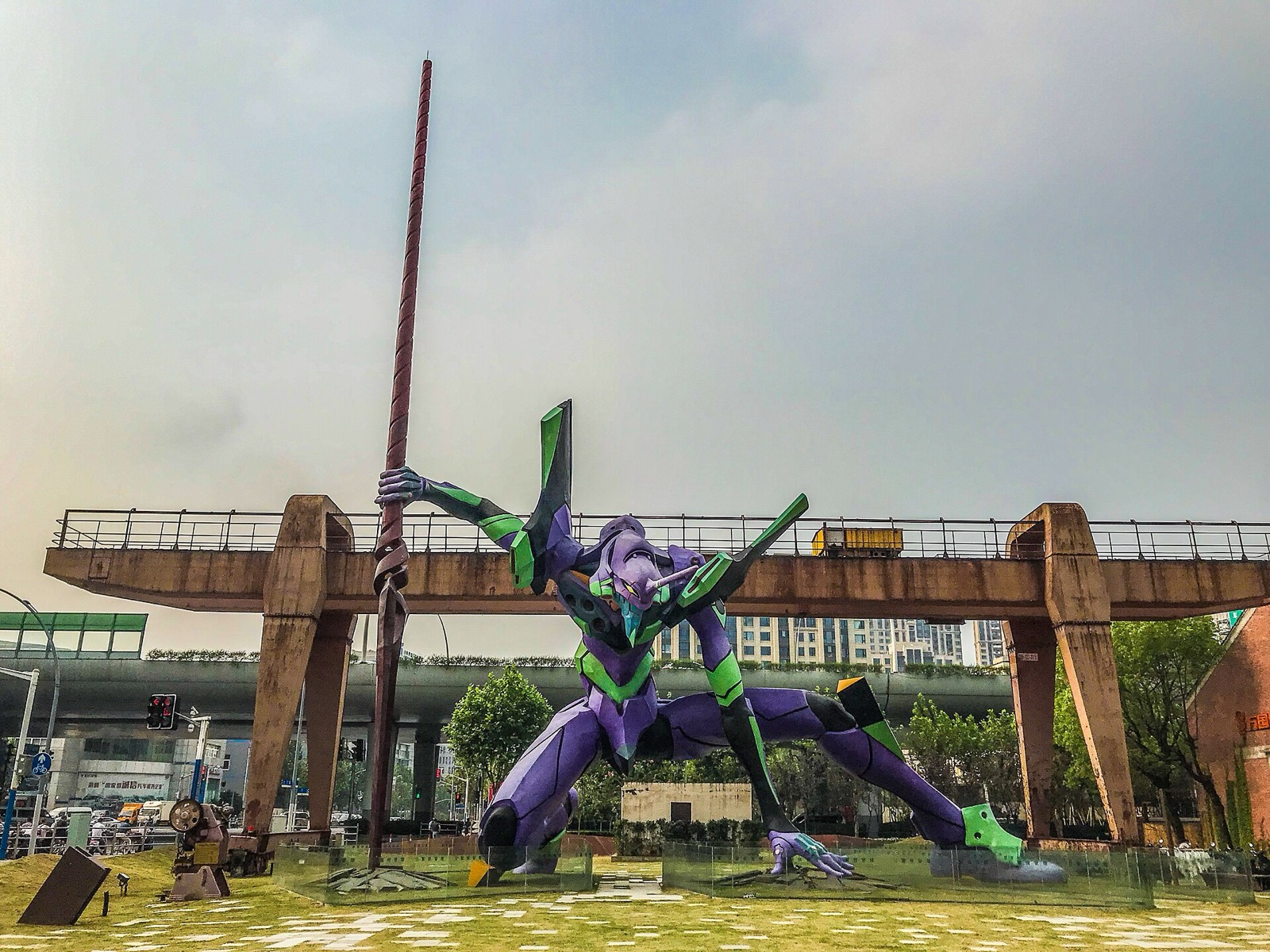 Purple and green EVA-01 robot statue holding a long spear in an outdoor plaza