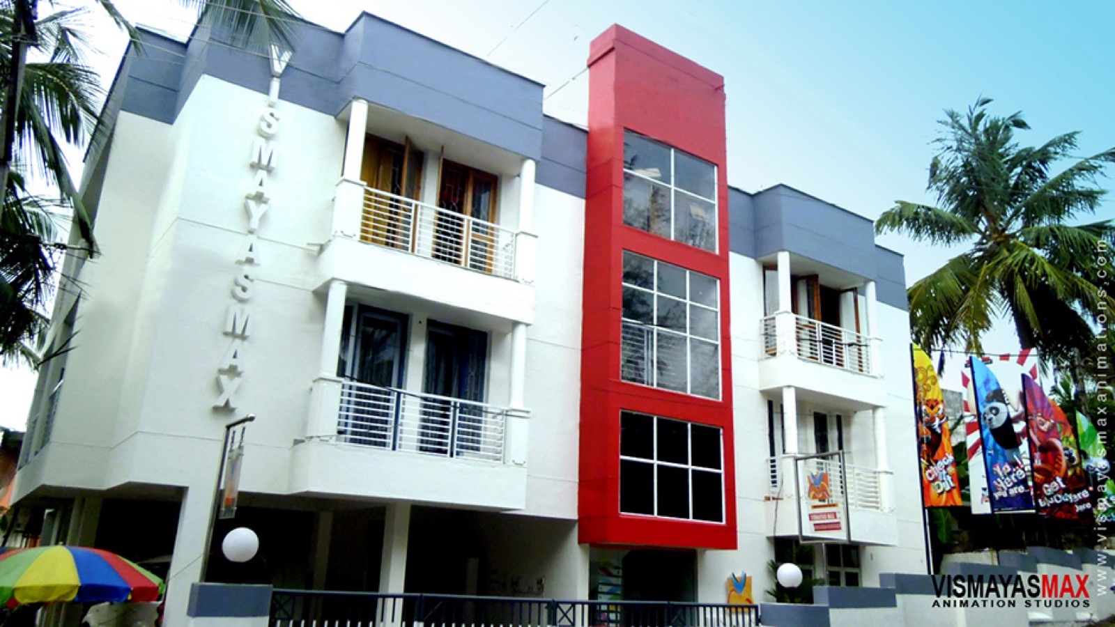 White three-storey animation studio building with a red glass tower and palm trees