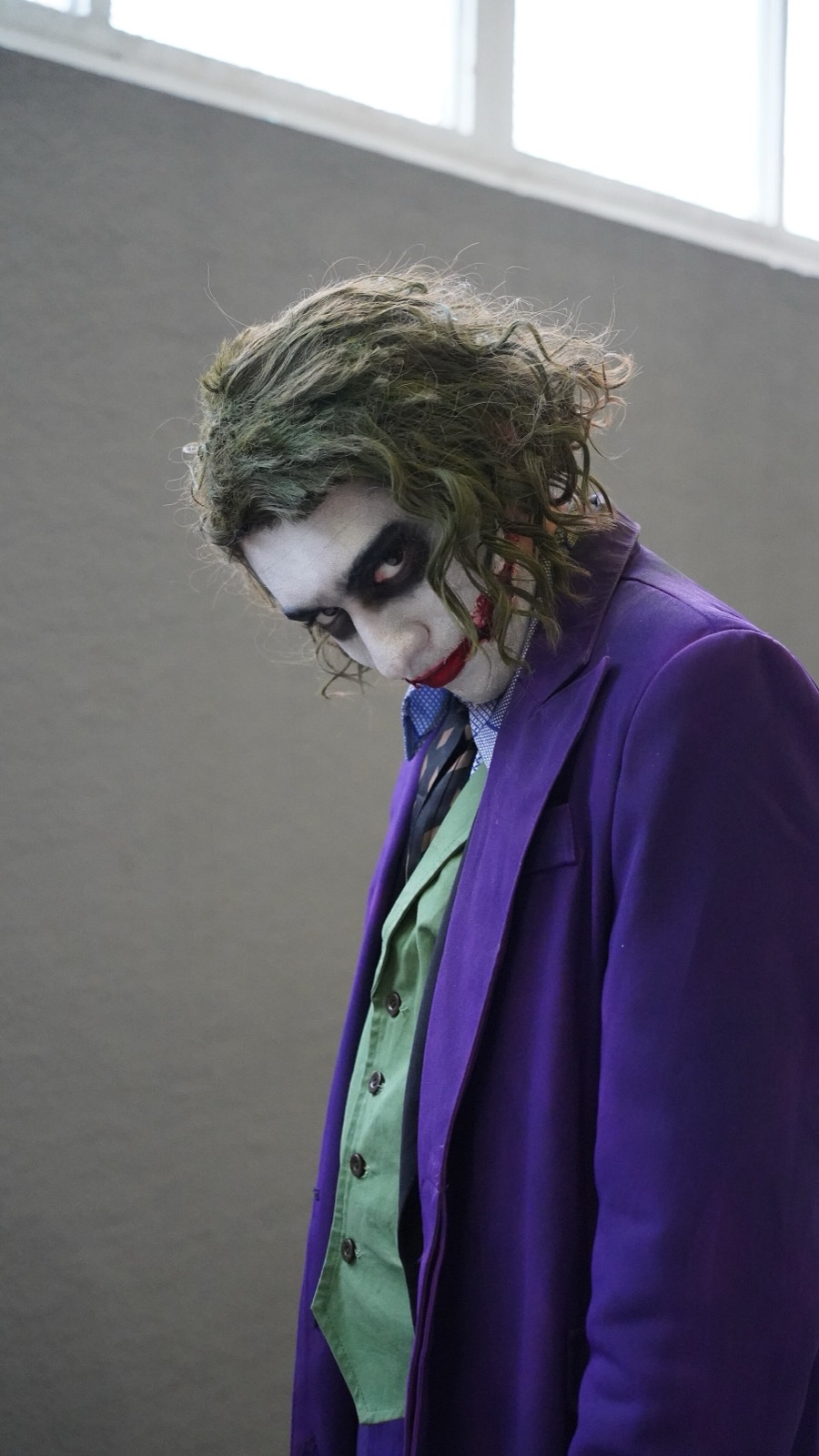 Cosplayer in Joker makeup, green hair and purple coat looking down at the camera
