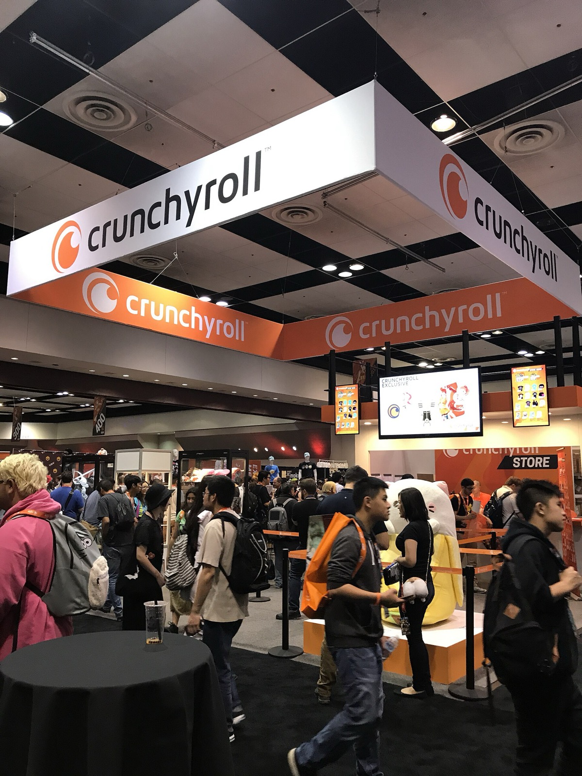 Convention hall with large orange and white Crunchyroll banners above a crowded booth