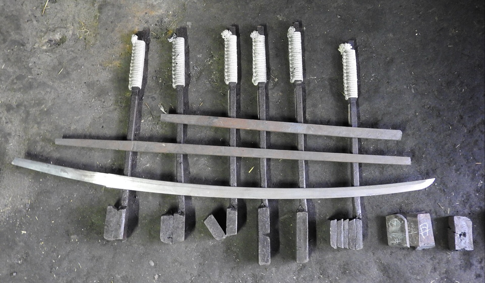 Steel billets, part-forged bars and a curved katana blade laid out on a workshop floor