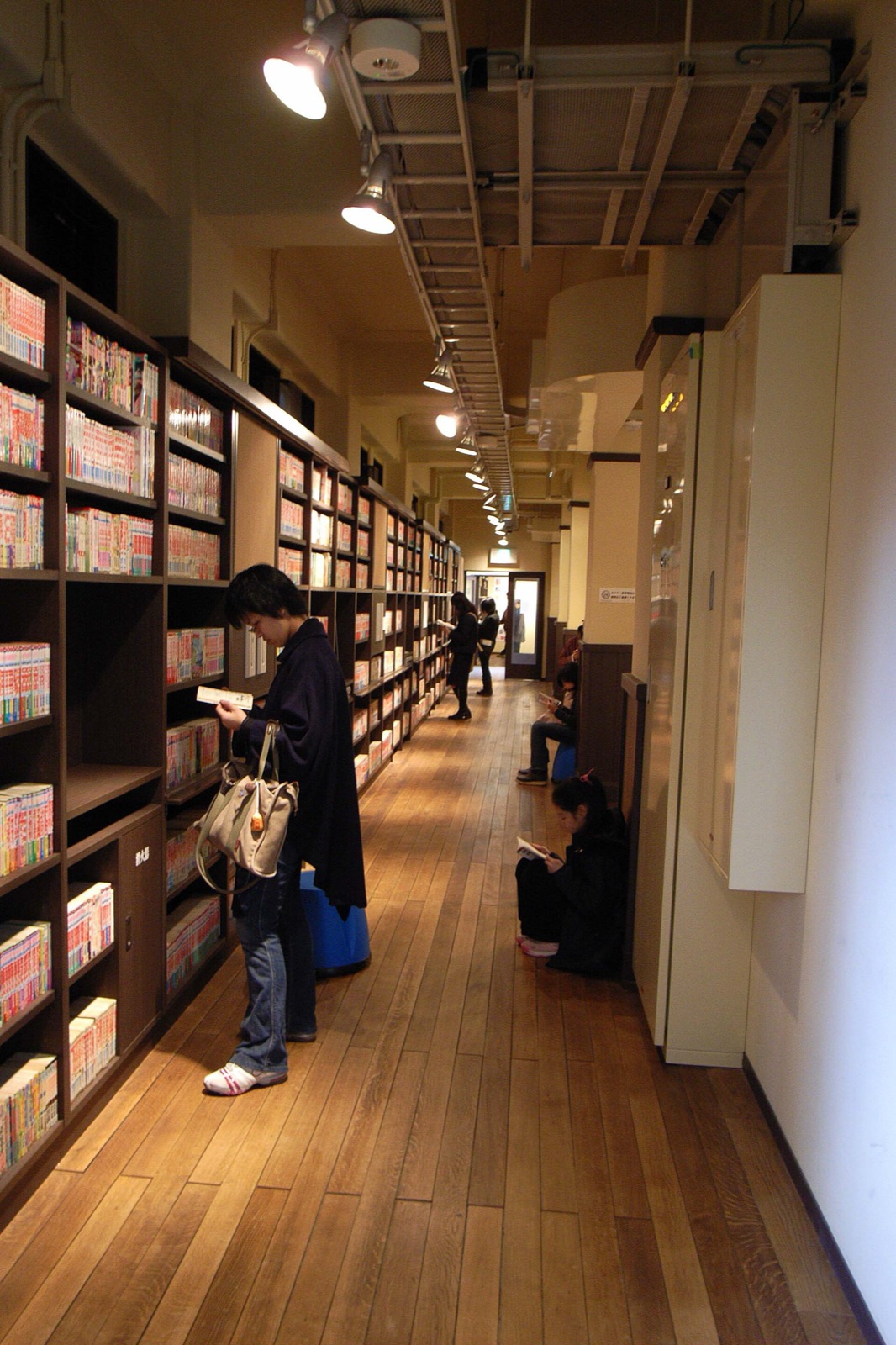Visitors reading beside tall wooden manga shelves in a corridor