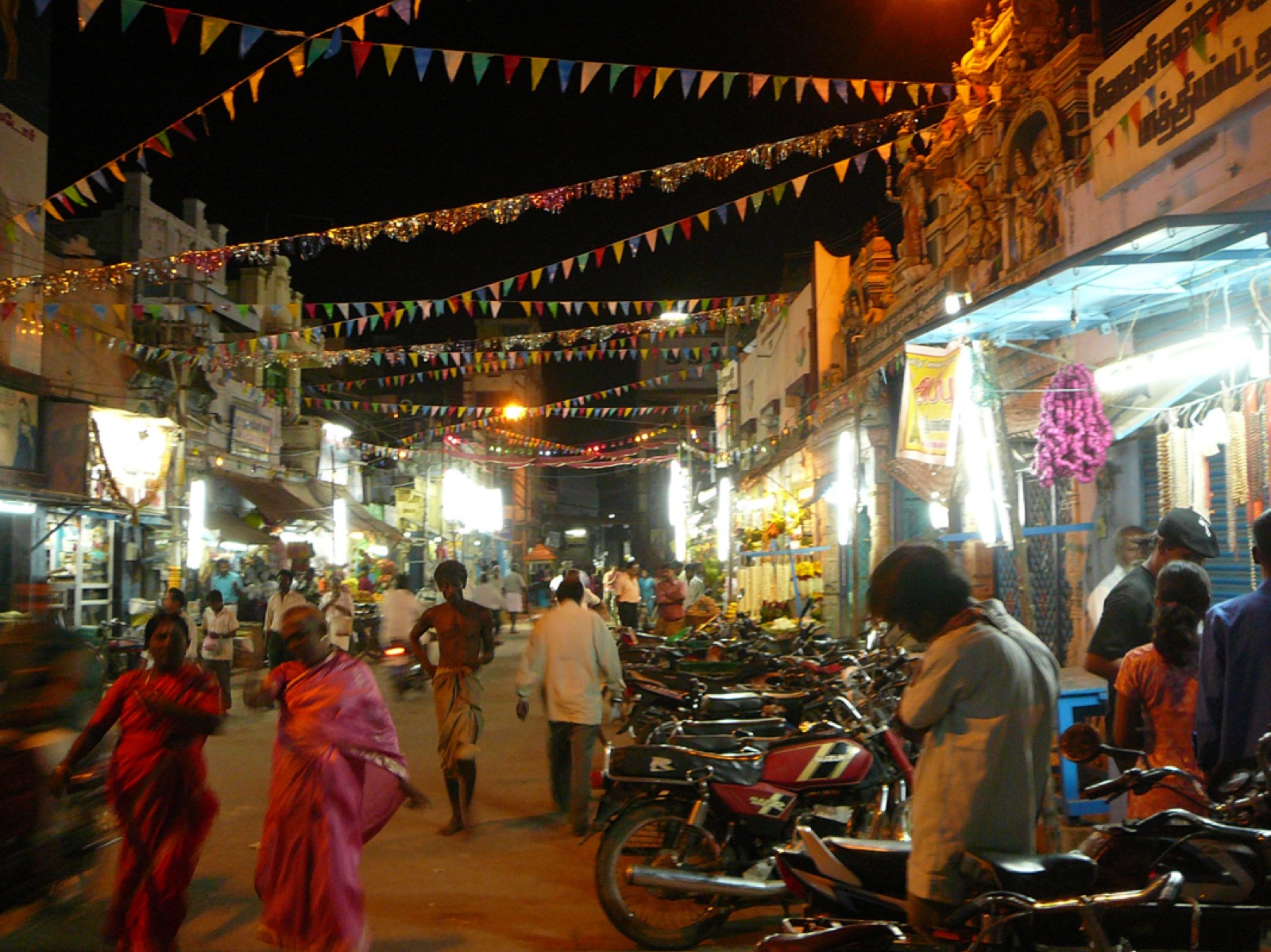 Crowded night street in Sivakasi with bunting, lit shops and parked motorbikes