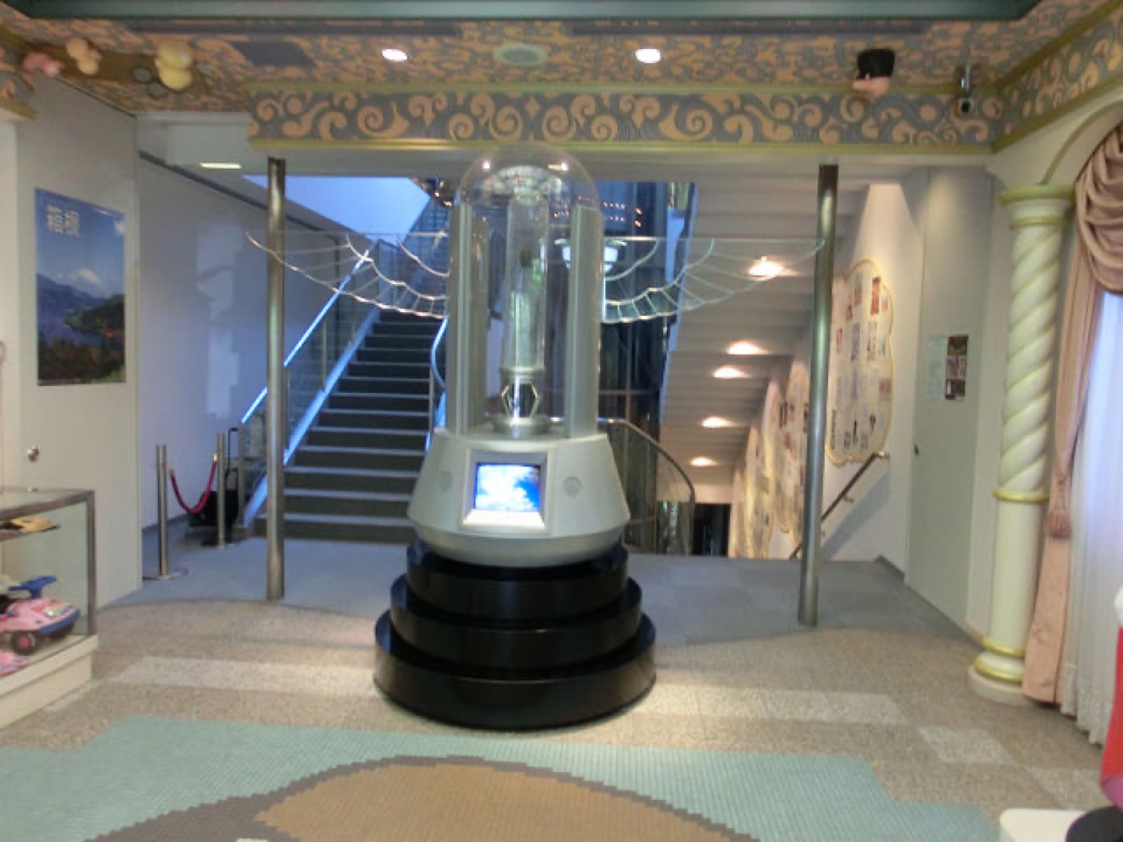 Museum lobby with a winged glass capsule display in front of a staircase