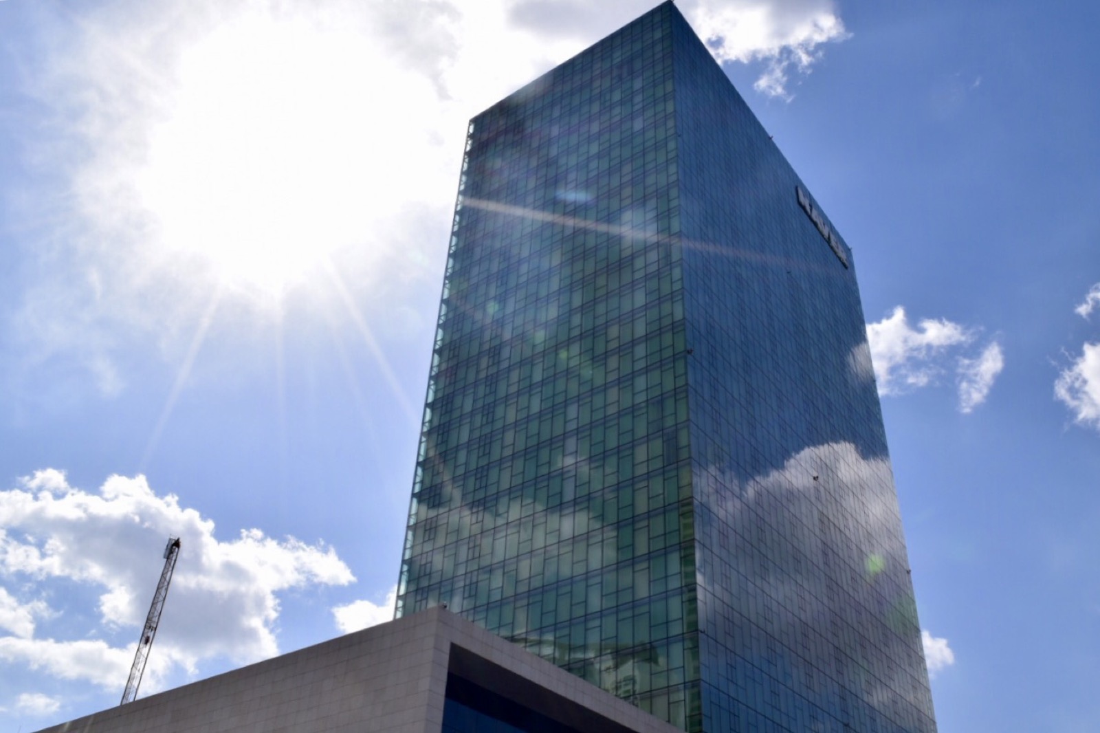 Green glass skyscraper headquarters under a bright sun and blue sky