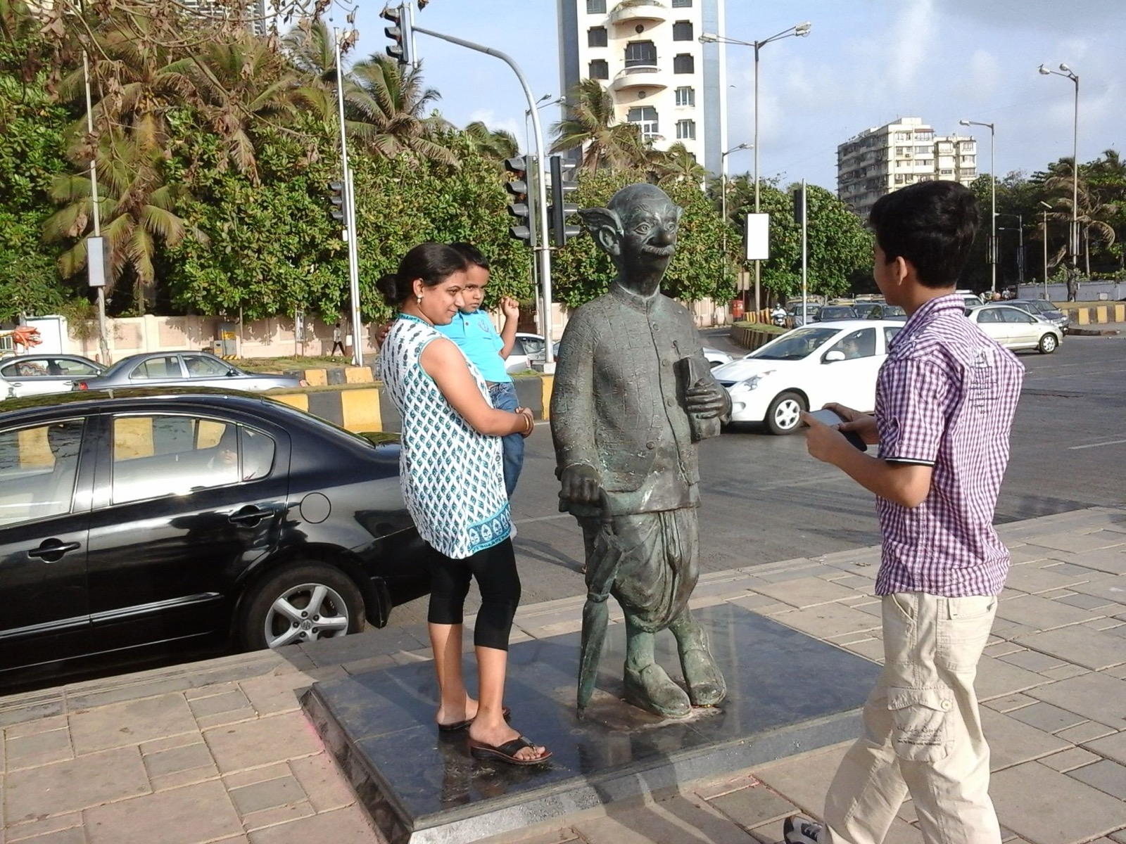 Bronze statue of the Common Man beside a busy Mumbai street, with passersby