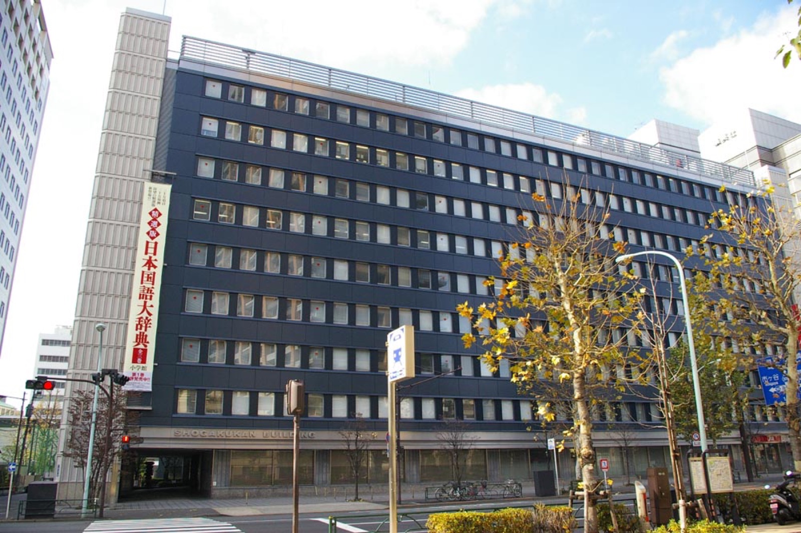 Dark office block with Shogakukan Building lettering above street trees