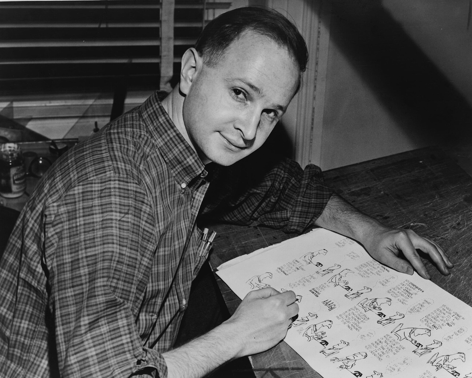 Black and white photo of a young Jules Feiffer drawing cartoons at a desk